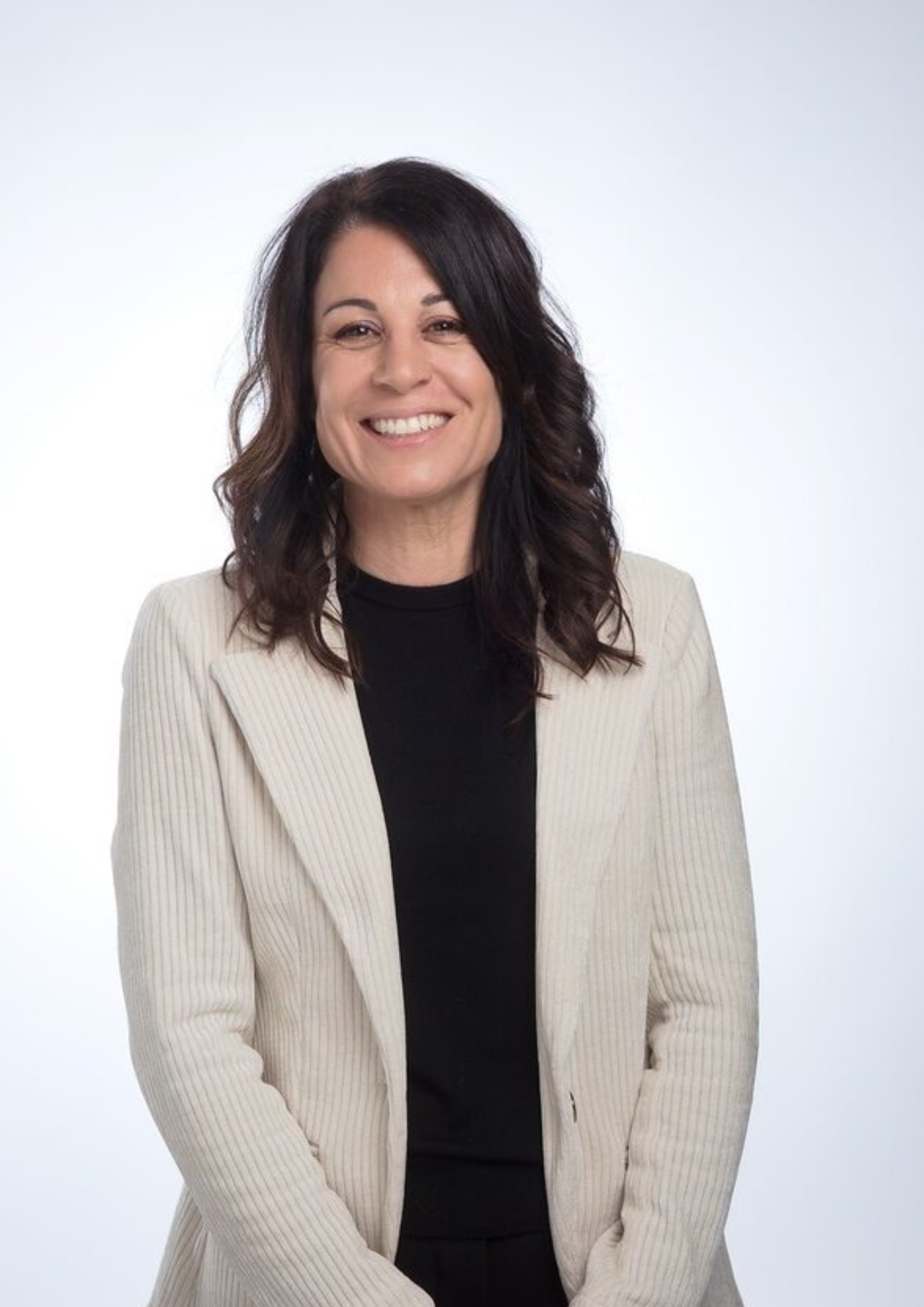 Professional woman in a light beige blazer and black top smiling in a studio portrait.