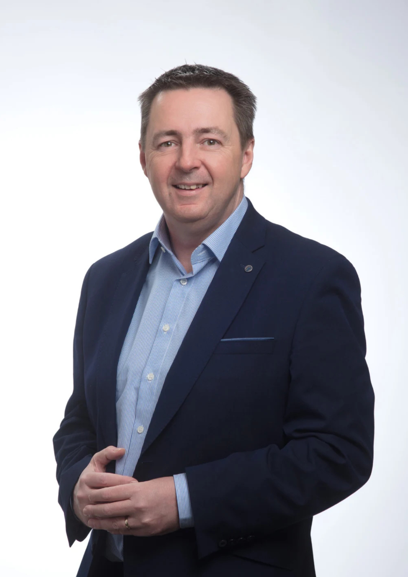 Professional man in a dark blue suit and light blue shirt smiling in a studio portrait.