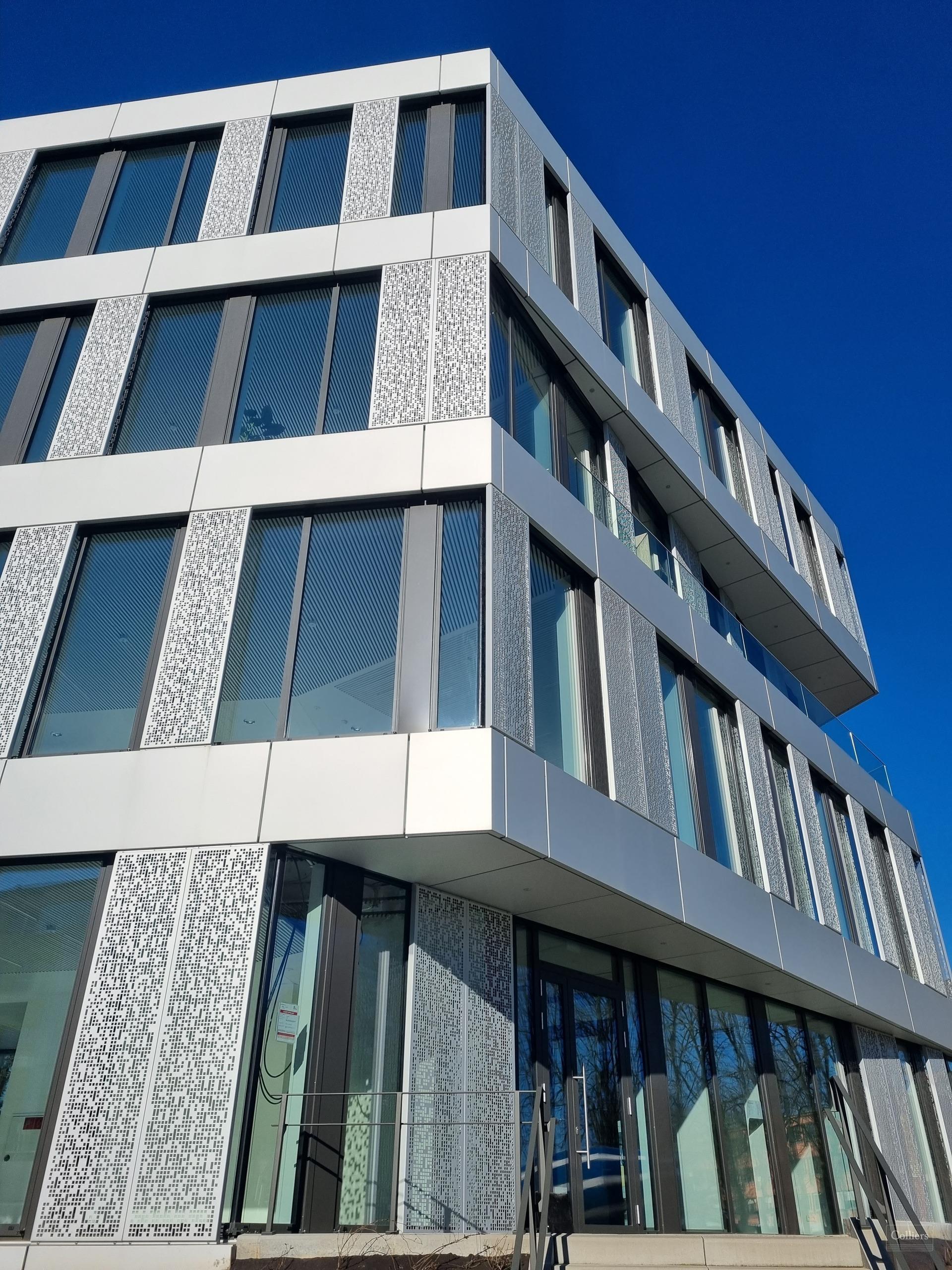 Modern office building with large glass windows and decorative white panels, photographed under a clear blue sky.